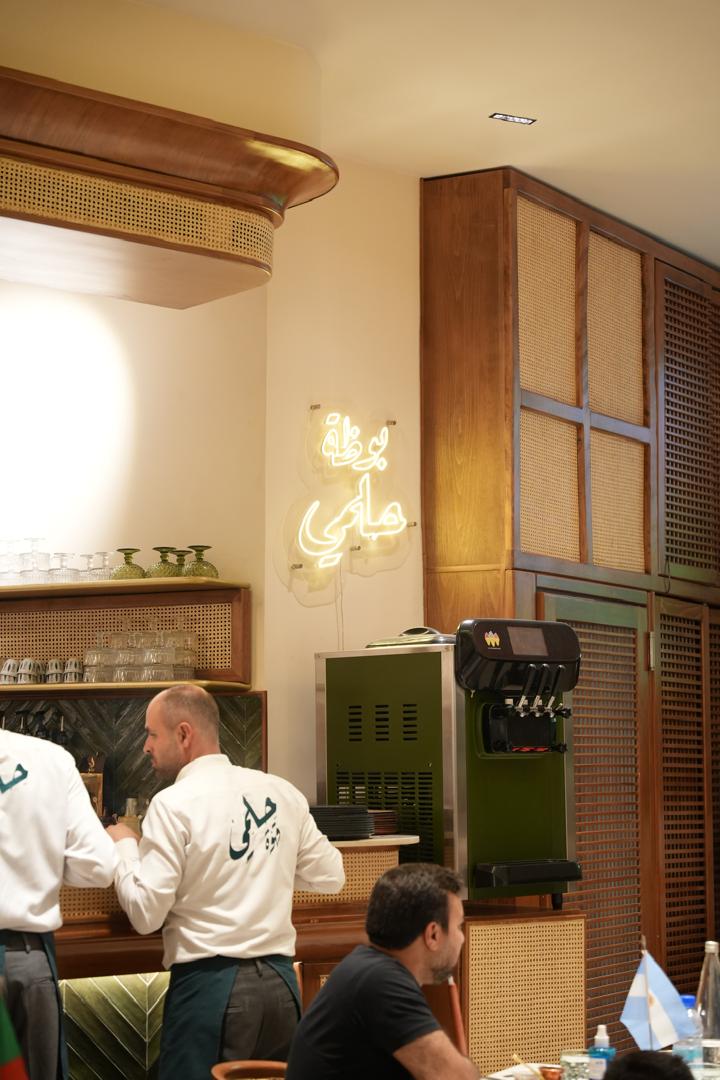 Helmi Cafe service counter with neon Arabic signage and rattan joinery